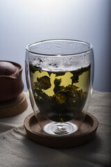 A green tea brew in a double glass cup on a linen cloth against white background