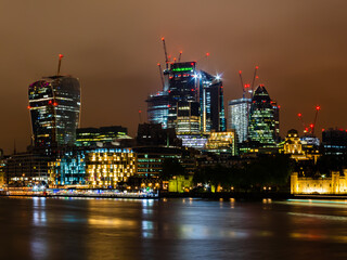 Fototapeta premium Skyline of London with its famous skyscrapers and in the foreground the Thames at night