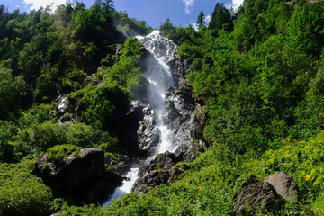 Fototapeta na wymiar high waterfall between rocks and green shrubs in the mountains
