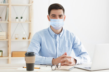 Young employee or teacher sitting in the office, wearing medical mask, practicing social distancing because covid safety protocol