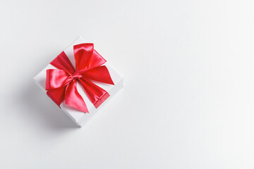 White present box tied with red beautiful bow on white background. Top view, copy space.