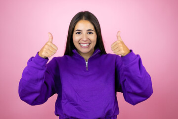 Young beautiful woman wearing sweatshirt over isolated pink background success sign doing positive gesture with hand, thumbs up smiling and happy. cheerful expression and winner gesture.