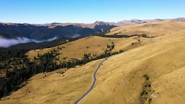 Aerial view of car driving down country road through rural rolling hills and mountain. High altitude road. Highway on the mountain. Mountain forest with fog and countryside asphalt road. Travel by car