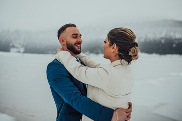 Bride and groom among snowy mountain. They are standing and hugging. Winter wedding outdoors. Close up.