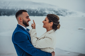 Bride and groom among snowy mountain. They are standing and hugging. Winter wedding outdoors. Close up.