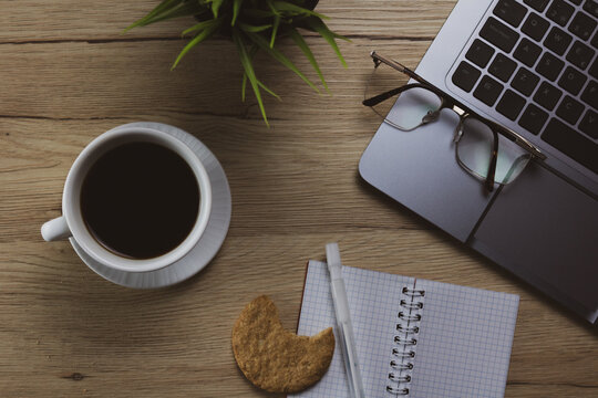 Top view modern office table desk with office supplies like laptop, eyeglass, cup of coffee and notes bloc. Desktop workspace. Wood texture background. 