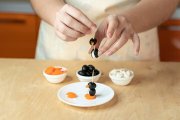 Woman’s hands preparing a healthy food
ingredients for making a skewer snack made from olives, curd cheese and carrots in the shape of a penguin