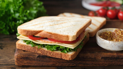Sandwich with ham, cheese, tomato and lettuce on a wooden table. Tasty healthy sandwich
