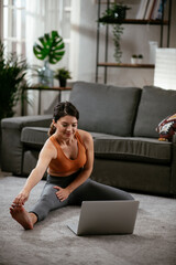 Athletic woman in sportswear doing stretching exercises at home in the living room. Fit woman training at home..