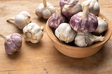 bunch of fresh garlic in a wooden plate on a brown table