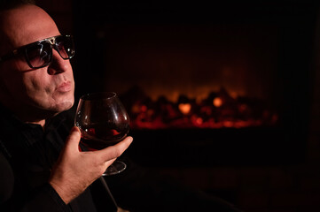 Mature man drinking cognac by the fireplace.