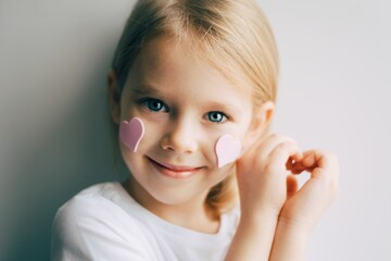 Pretty blonde girl show heart shape symbol with hands. Child and valentines day. Love. Pink hearts on a face. - 403785537