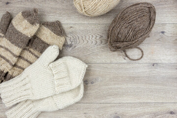 Fototapeta na wymiar Skeins of thread and knitted mittens on a wooden background. Mittens with a flap. The concept of hobby, home production and individual entrepreneurship.