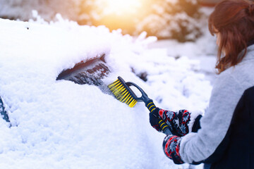 Young woman cleaning snow from windshield, scraping frozen ice.