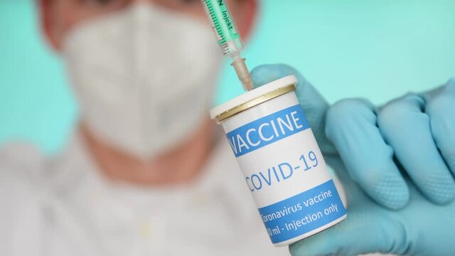 Closeup of a researcher with face mask and blue gloves filling a syringe with coronavirus vaccine.
