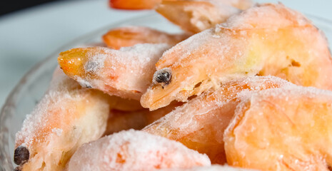 Raw frozen shrimp in a glass plate close-up.