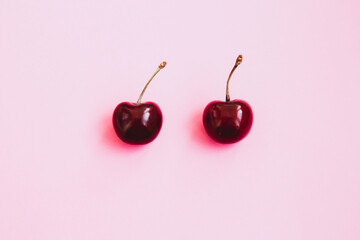 Two ripe cherries on a light pink background. Valentine's Day concept. Close-up of cherries. Summer background