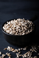 Peeled sunflower seeds in ceramic bowl on dark background.