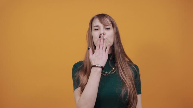Sending sweet air kiss blowing red lips stretching hand for taking selfie demonstrate feelings. Young attractive woman, dressed green shirt blonde hair, yellow background