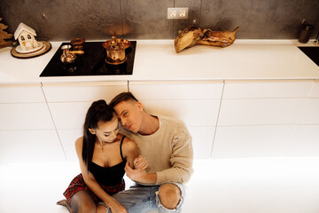 Lovely couple sit at the kitchen, cuddling and smiling. Gorgeous woman with attractive man cooking dinner, spend weekends together at home, enjoy tenderness, happiness concept