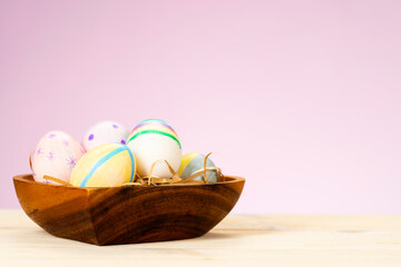 Colorful easter eggs in wooden plate on table on pink background