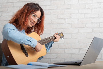 Fototapeta na wymiar Caucasian woman remotely teaches guitar playing on laptop. Online music training