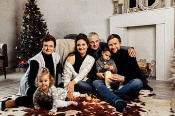 Beautiful portrait of happy family sitting near Christmas tree. Mature woman and man and young adult parents with little kids celebrate Christmas. Grandparents spend winter holidays with grandchildren