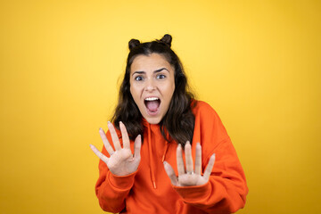 Young beautiful woman wearing sweatshirt over isolated yellow background afraid and terrified with fear expression stop gesture with hands, shouting in shock. Panic concept.