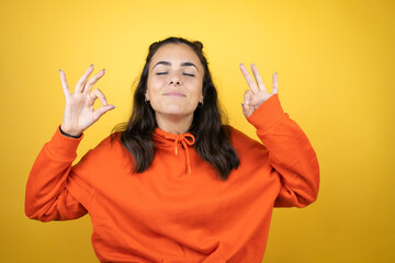 Young beautiful woman wearing sweatshirt over isolated yellow background doing ok sign with fingers and smiling, excellent symbol