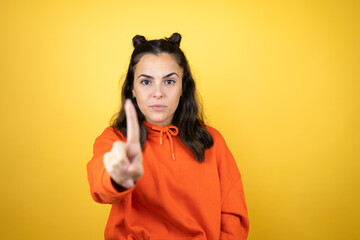 Young beautiful woman wearing sweatshirt over isolated yellow background showing and pointing up with fingers number one while is serious