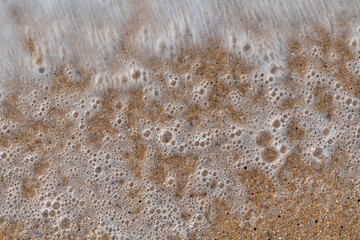 Fototapeta na wymiar Close up sea water waves with bubbles on sand beach. Pattern and texture surface with white and orange colors. Abstract outdoor natural view as a background.