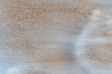 Close up sea water waves with bubbles on sand beach. Pattern and texture surface with white and orange colors. Abstract outdoor natural view as a background.