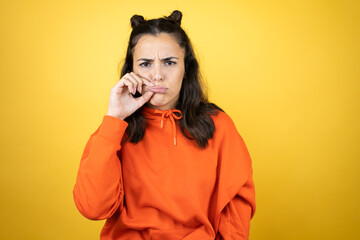 Young beautiful woman wearing sweatshirt over isolated yellow background mouth and lips shut as zip...