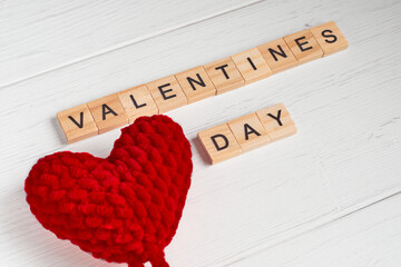 Top view of the word valentines day laid out from square wooden tiles and red big knitted ahearts on old white wooden background. Selective focus
