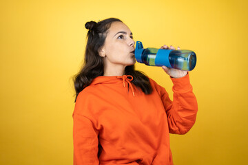 Young beautiful woman wearing sweatshirt holding a water bottle over isolated yellow background drinking water