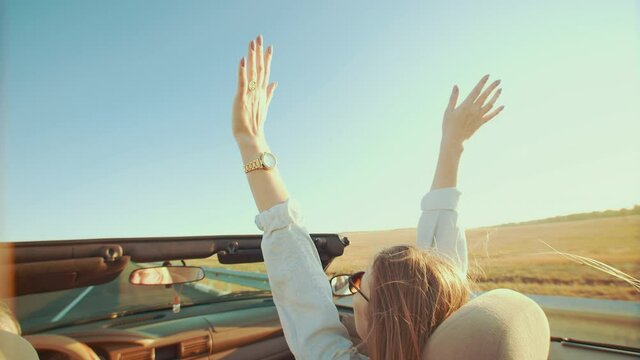 Lifestyle, concept of freedom. Happy woman in front seat of convertible raises her hands up, enjoying life, against sky. Closeup of raised hands of woman driving car without roof.
