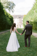 Fototapeta na wymiar Stylish young wedding couple cheerfully posing on the alley against the backdrop of the palace.