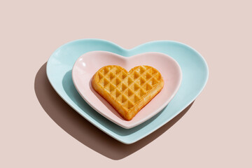 Heart shaped  belgian waffles on blue plate on pink background. Happy Valentine's Day. Close-up.