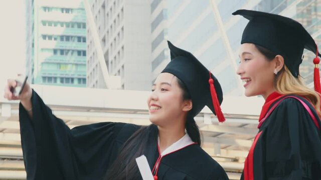 Young asian women in graduation gown outfit meeting outdoor and take a selfie together with smile and happiness in university graduated event