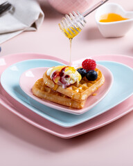 Heart shaped  belgian waffles with Ice-cream and berries on pink background. Tasty breakfast. Close-up.