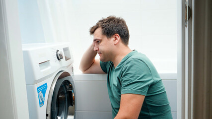 Portrait of young man struggling and getting confused while setting washing machine for laundry