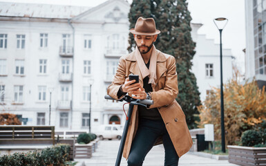 On the electric scooter. Young male model in fashionable clothes is outdoors in the city at daytime