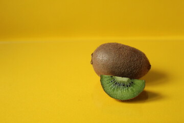 A trendy still life of a kiwi and a piece of fruit lie on the Illuminatiited yellow background with...
