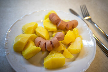 Sausages and potatoes on a white plate on the table, next to a knife and fork
