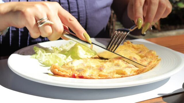 Brunette woman eat omelet with fork and knife in a cafe on the street