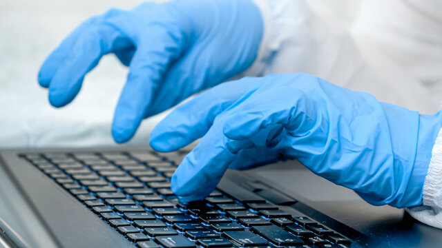 Closeup of fingers in medical gloves typing on laptop keyboard. People working from home and protecting from covid-19