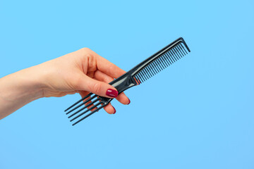 Female hand holding hair comb against blue background