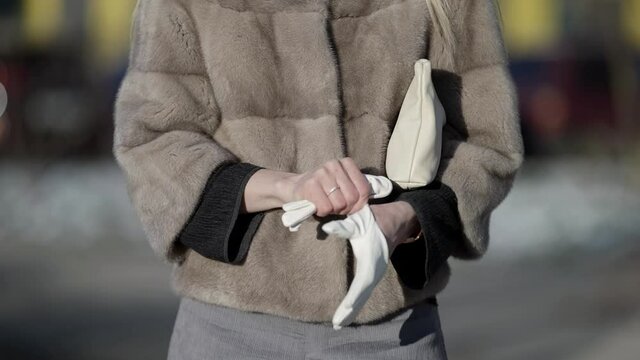 A young woman in a mink coat walks on the street of the city. Puts gloves on his hands. Winter fashion.