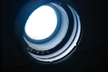 Close up image of a vintage film and slide projector lens on a dark background.