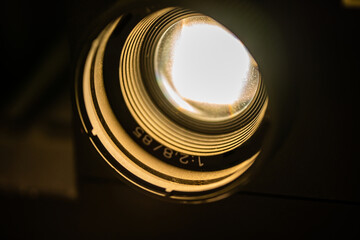 Close up image of a vintage film and slide projector lens on a dark background.